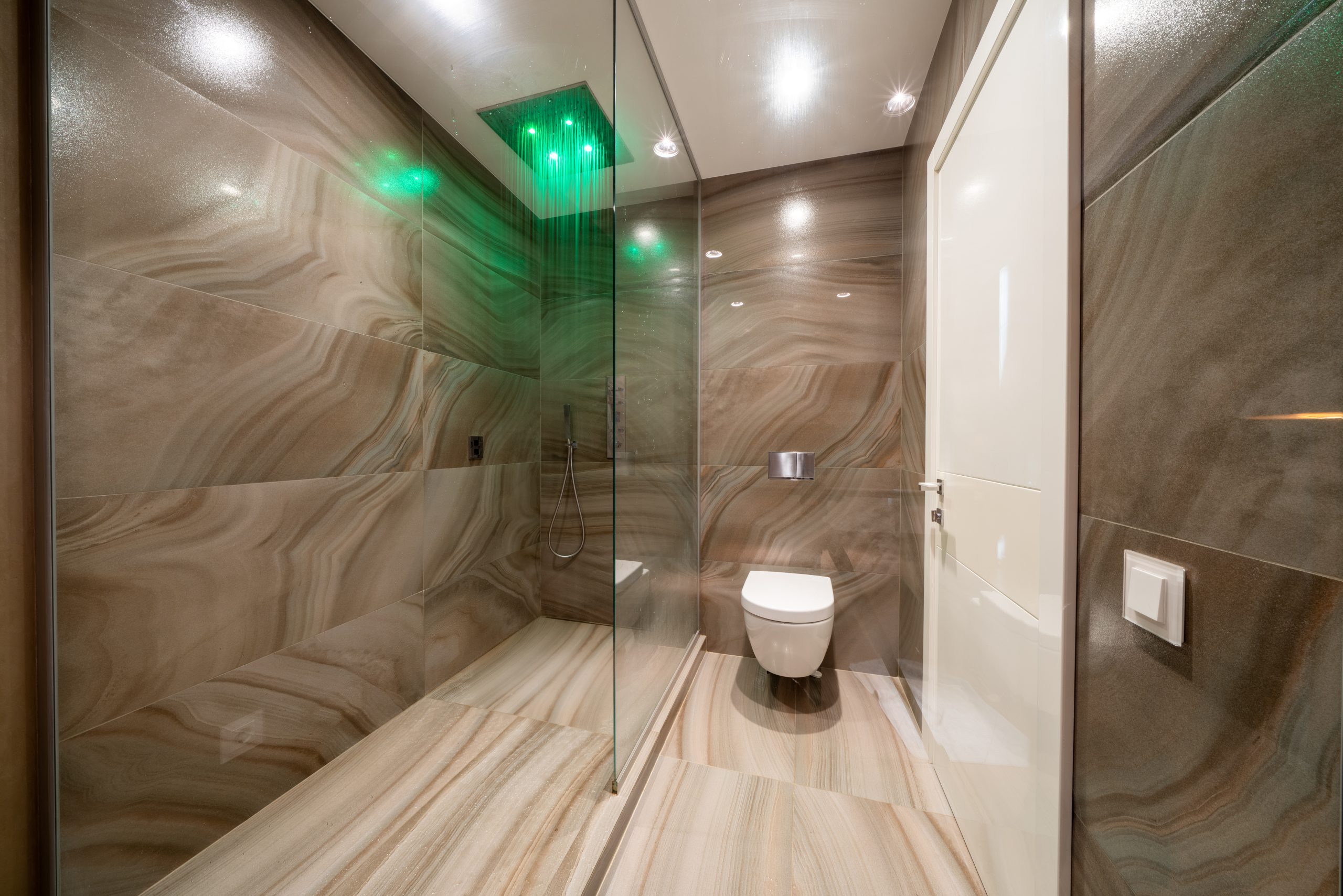Shower and toilet in contemporary bathroom designed in minimal style in apartment. Hotel, apartment or home interior design. Standard modern bathroom with shower separated with glass wall
