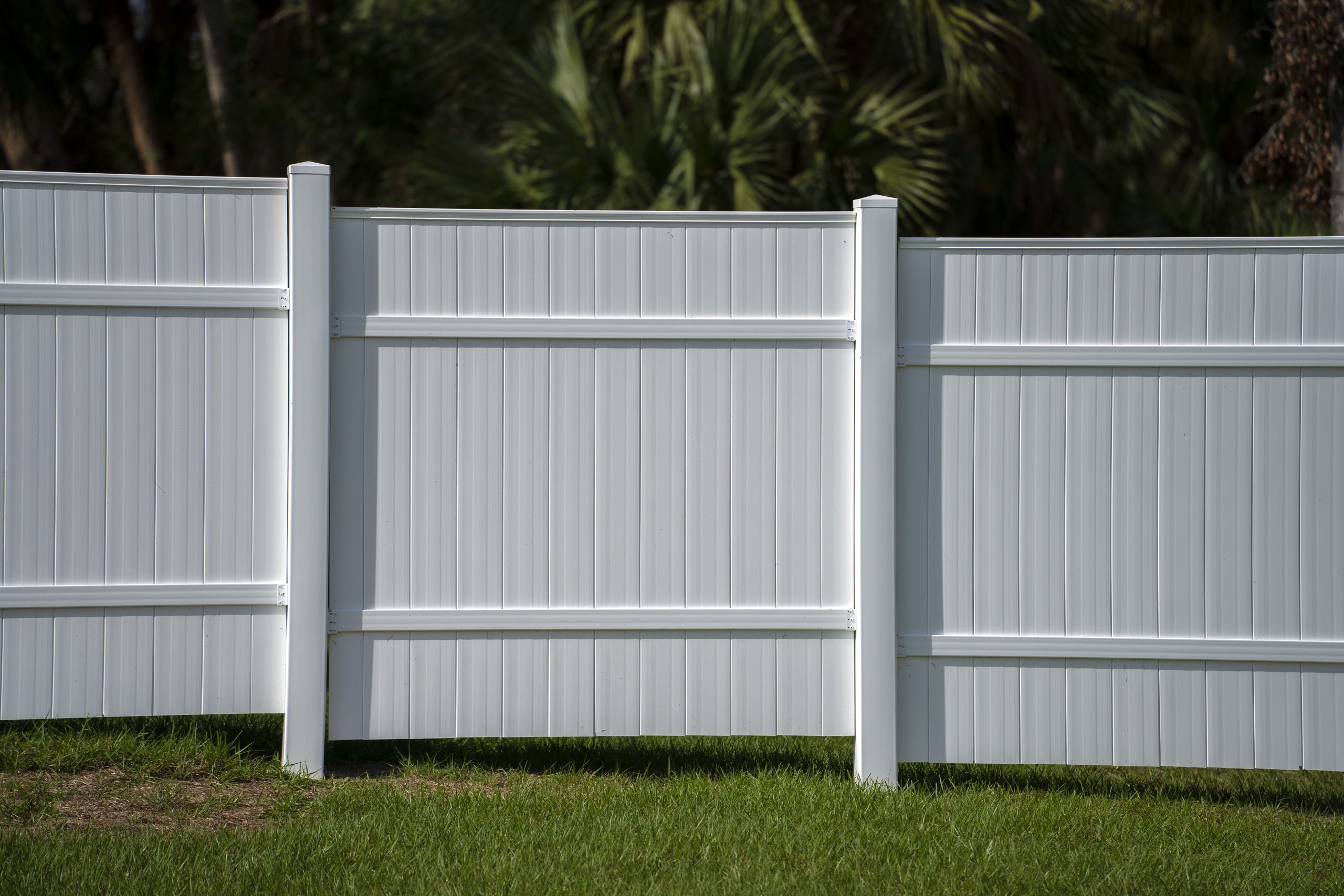 White vinyl picket fence on green lawn surrounding property grounds for backyard protection and privacy